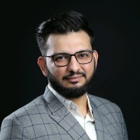 Profesyonel bir görünümdeki adam, siyah arka planda fotoğraflanmış. Okunur metin yok.